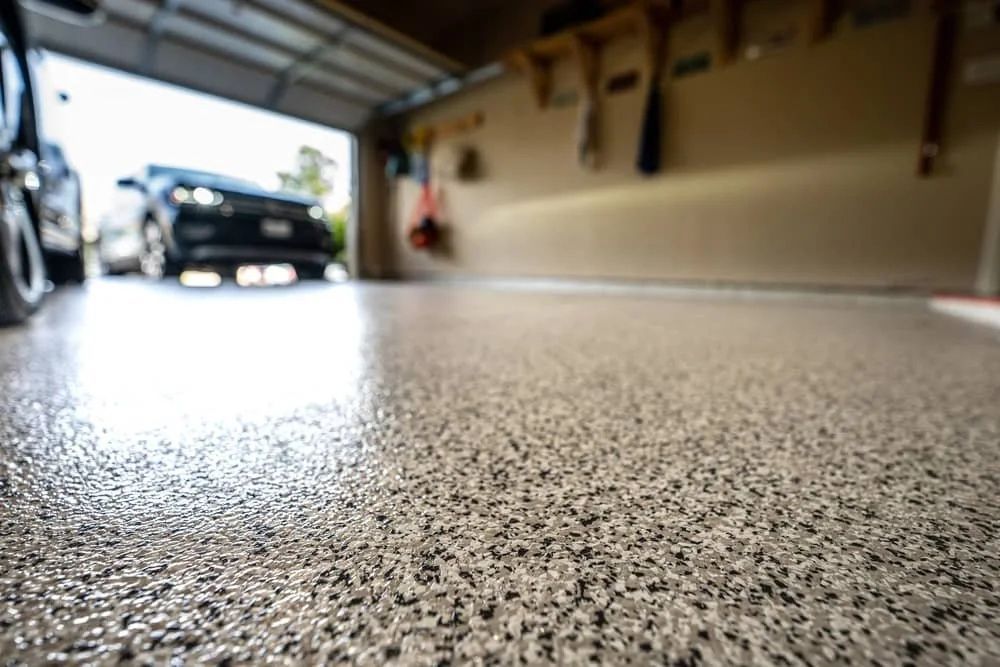 Commercial kitchen with stainless steel countertops, sinks, and beige speckled flooring.