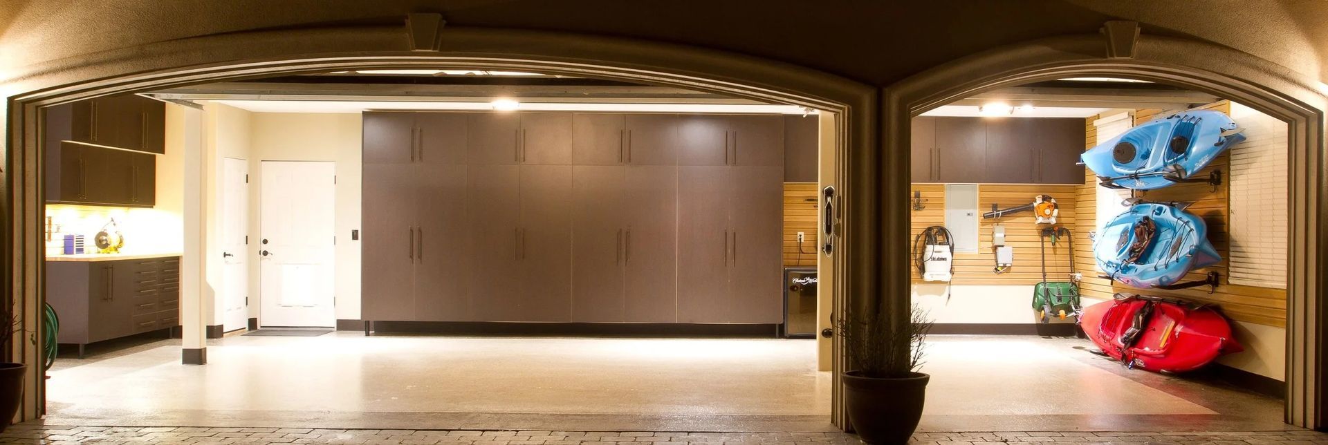 A well-lit garage interior with storage cabinets, a door, and kayaks.