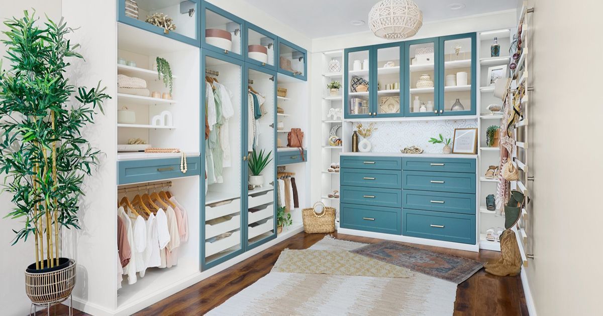 Bright walk-in closet with blue cabinets, mirrored doors, shelves, and hanging clothes on a light rug.