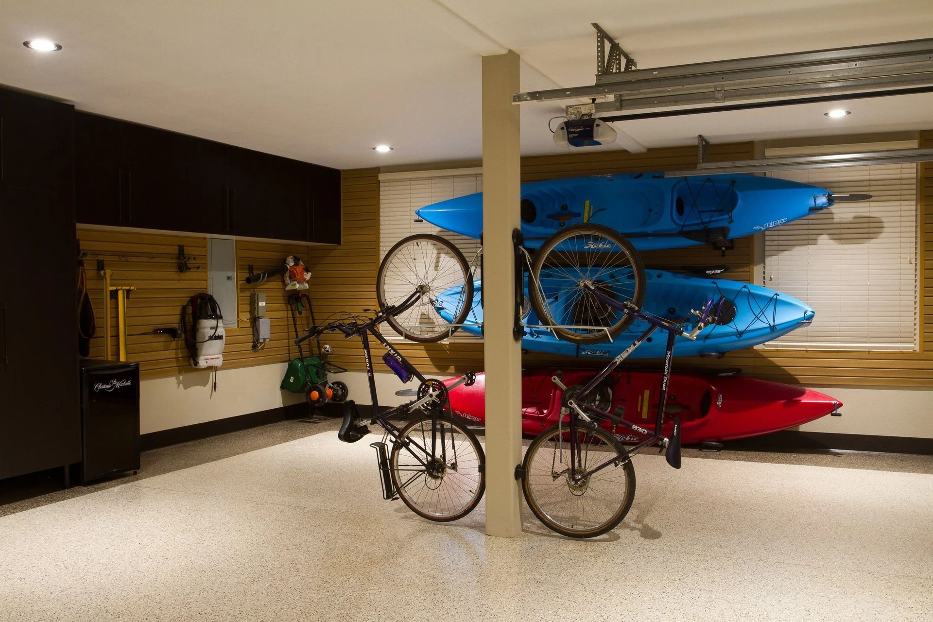 Garage with storage; kayaks and bikes hanging; speckled floor; neutral tones.