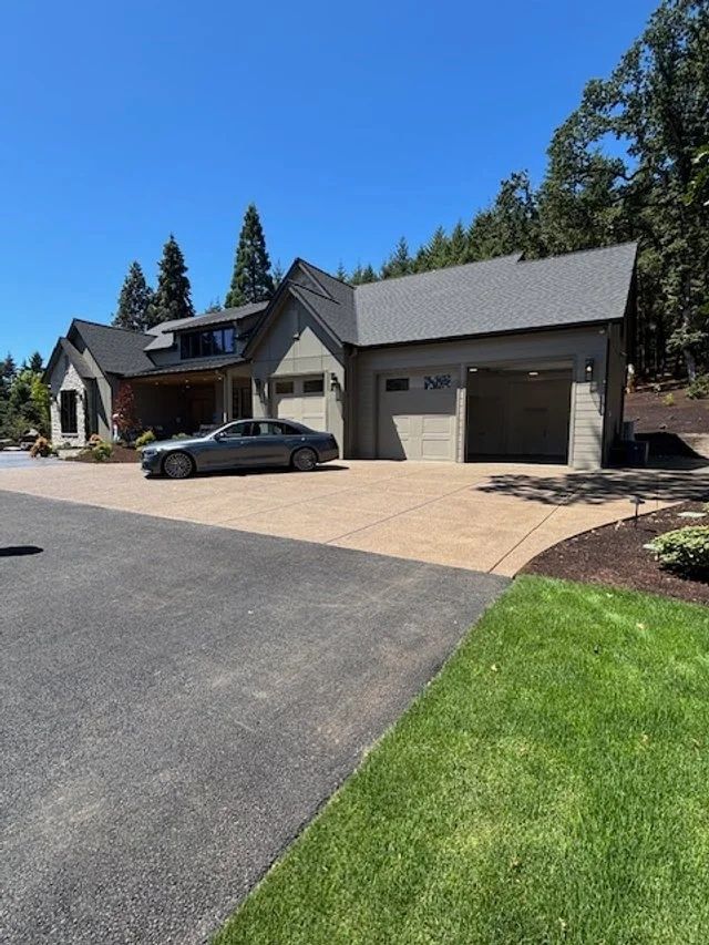 A gray house with attached garage, a car in the driveway, and a paved entrance on a sunny day.