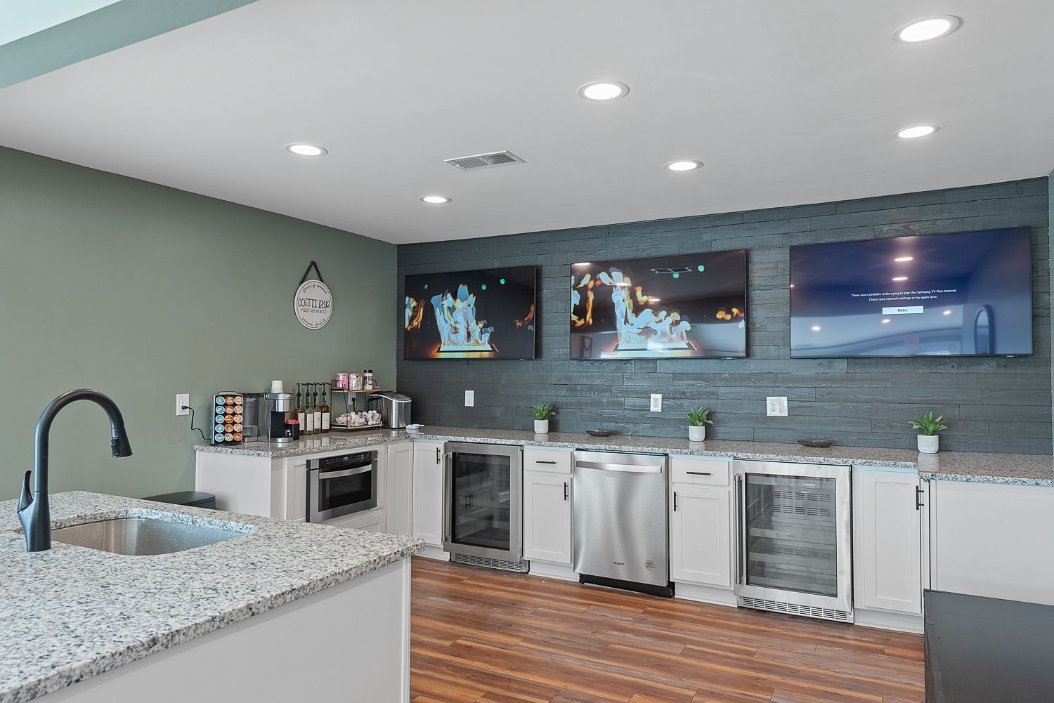 A kitchen with granite counter tops , stainless steel appliances , and a large flat screen tv.