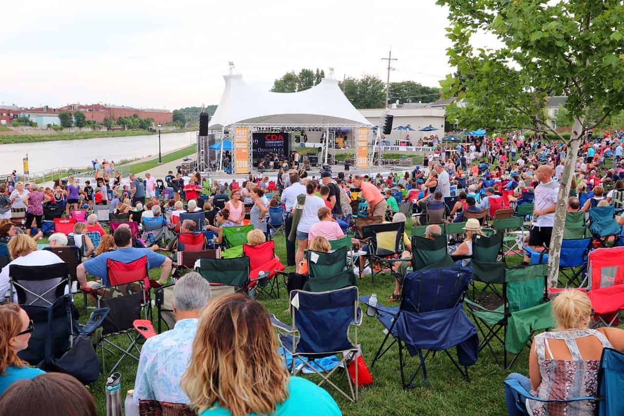 A large crowd of people are sitting in chairs in front of a stage at a concert.