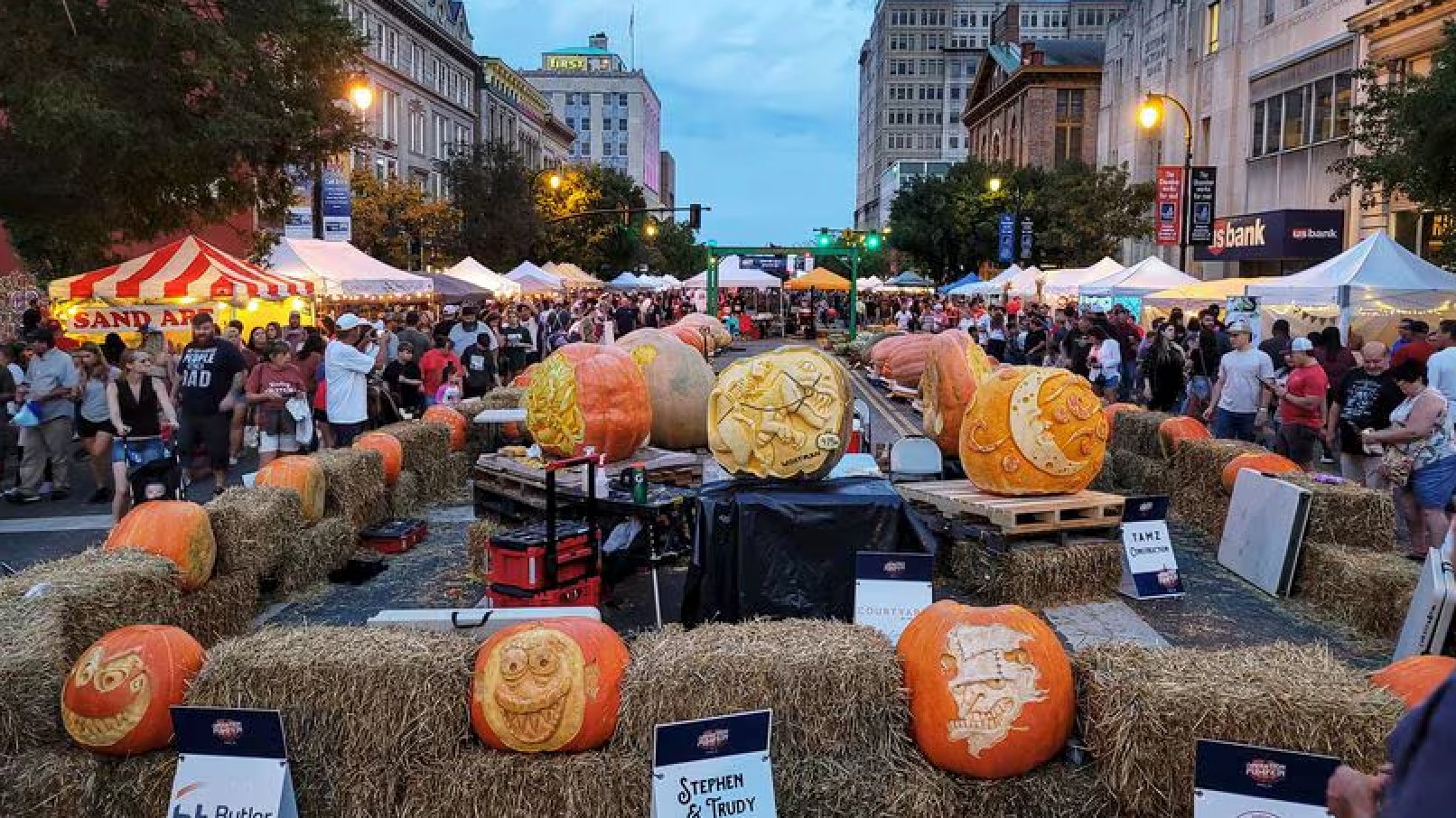 A bunch of pumpkins are sitting on hay bales on a city street.