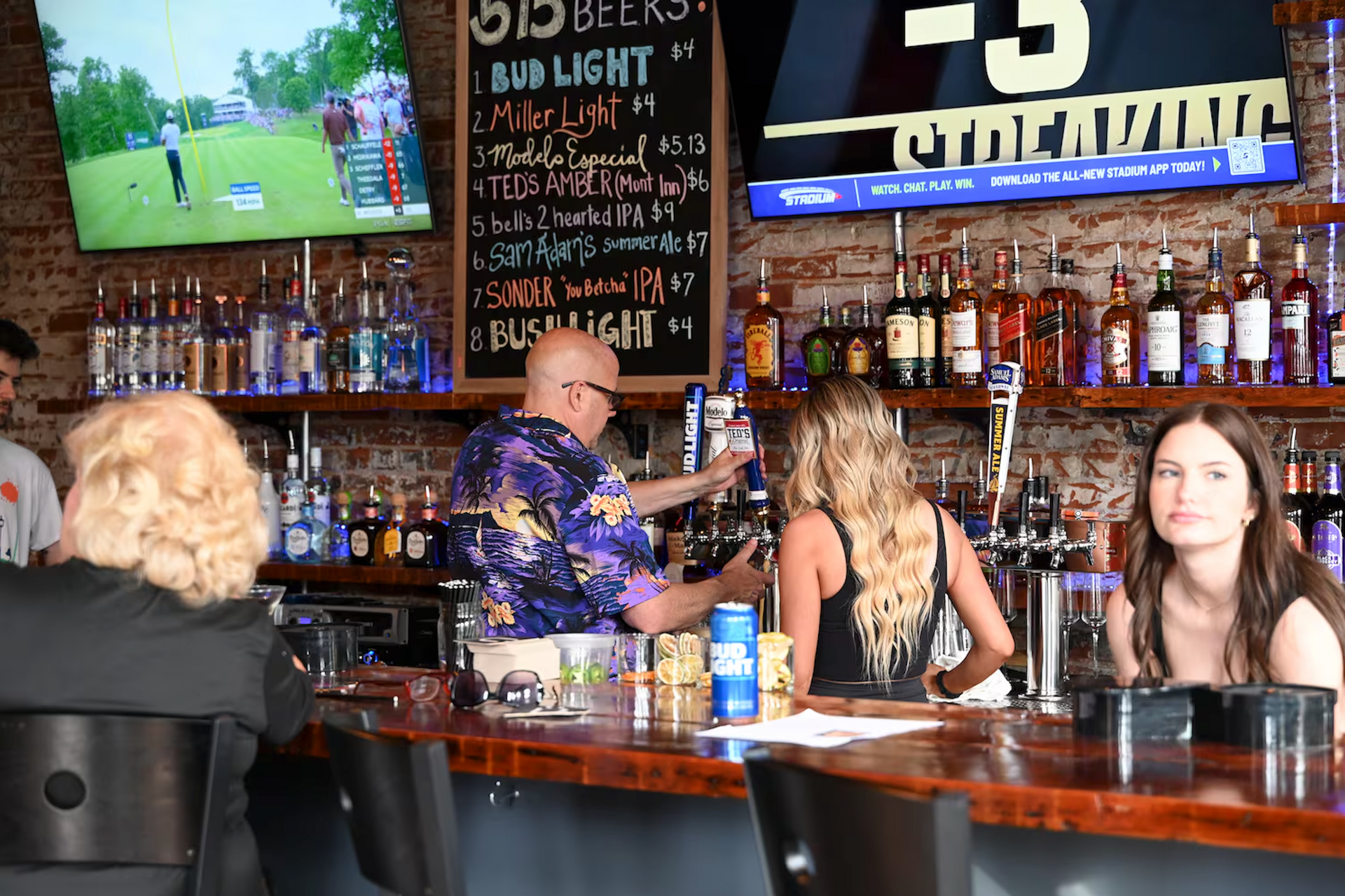 A group of people are sitting at a bar with a sign that says bud light on it.
