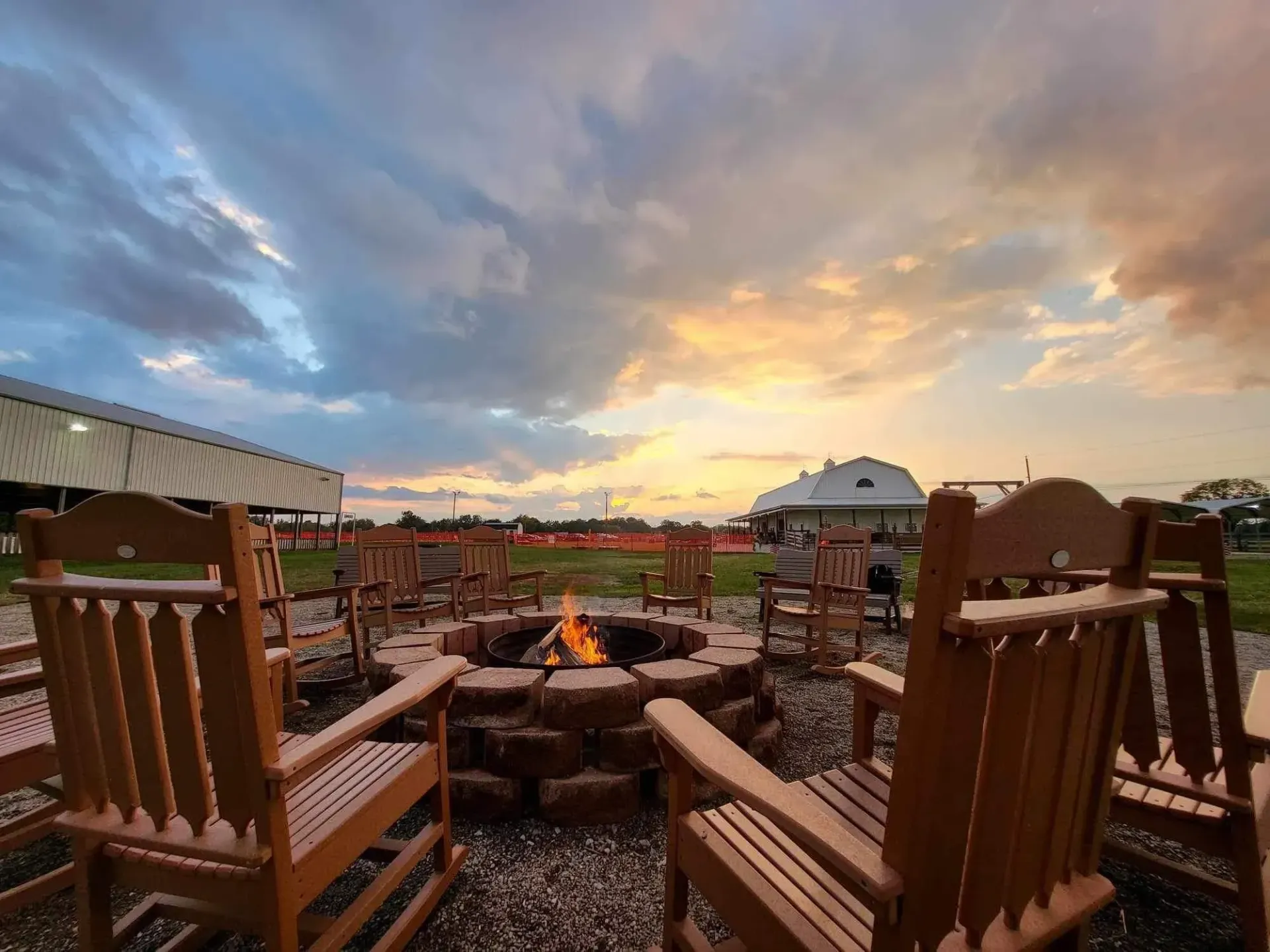 A group of rocking chairs are sitting around a fire pit at sunset.
