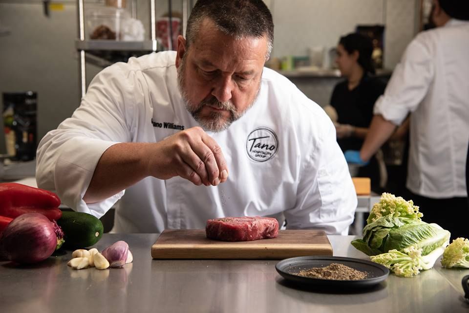 A chef is preparing a steak on a cutting board in a kitchen.