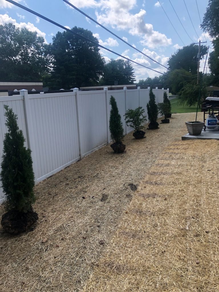 A white fence with trees in front of it in a yard.