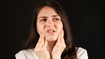 Woman touching her jaw and cheek with a worried expression on a black background
