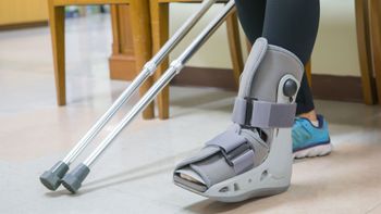 Person with foot brace using crutches indoors on a light floor
