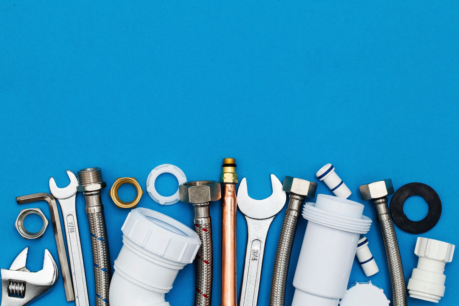Assorted plumbing tools and fittings arranged on blue background, including wrenches and pipes.