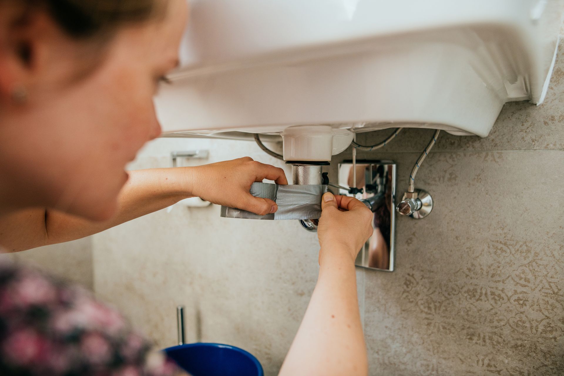 Woman trying to fix a leak in a sink using strong tape.
