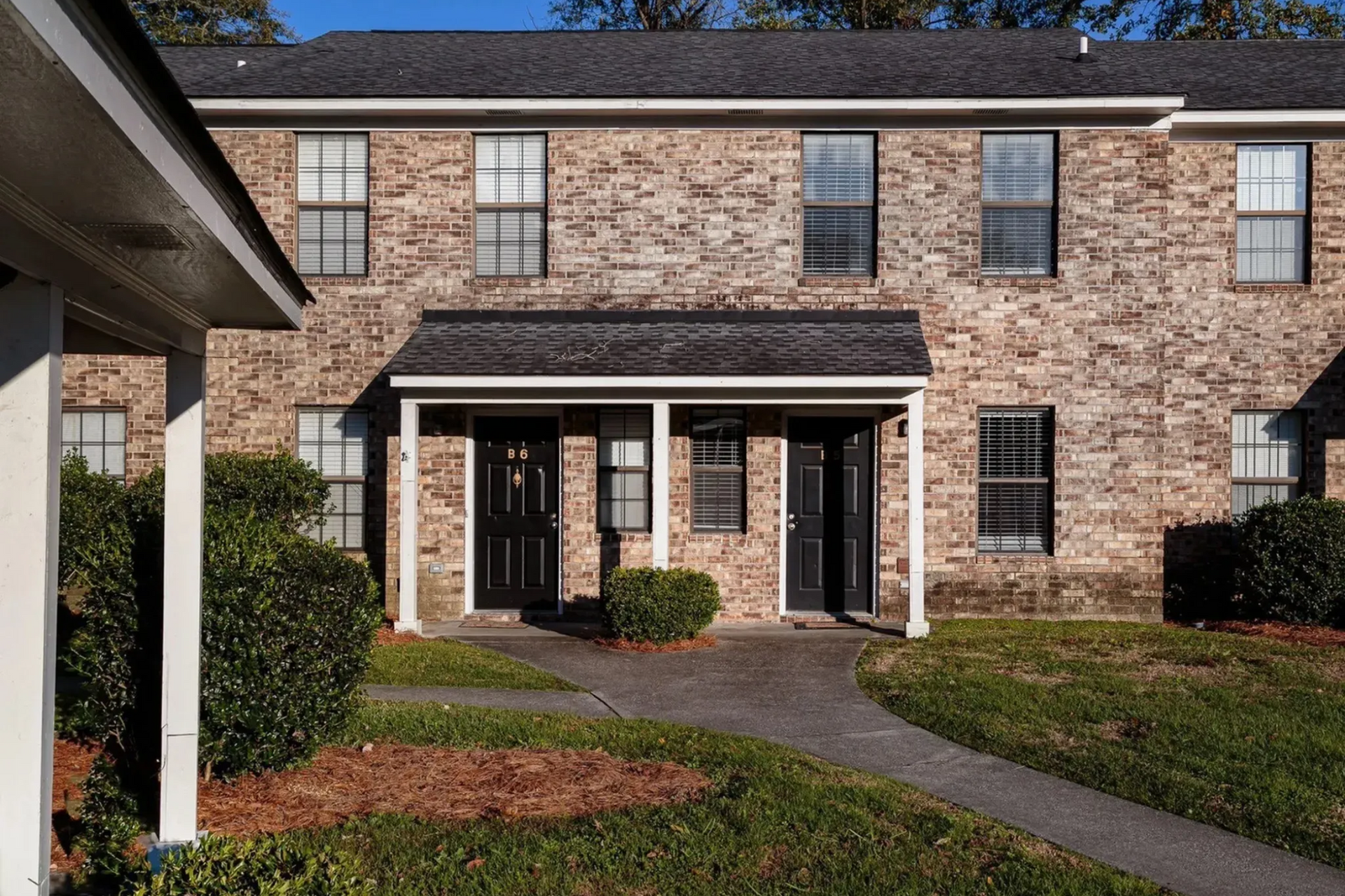 Exterior view of a two-story brick apartment building with a pathway and landscaping.