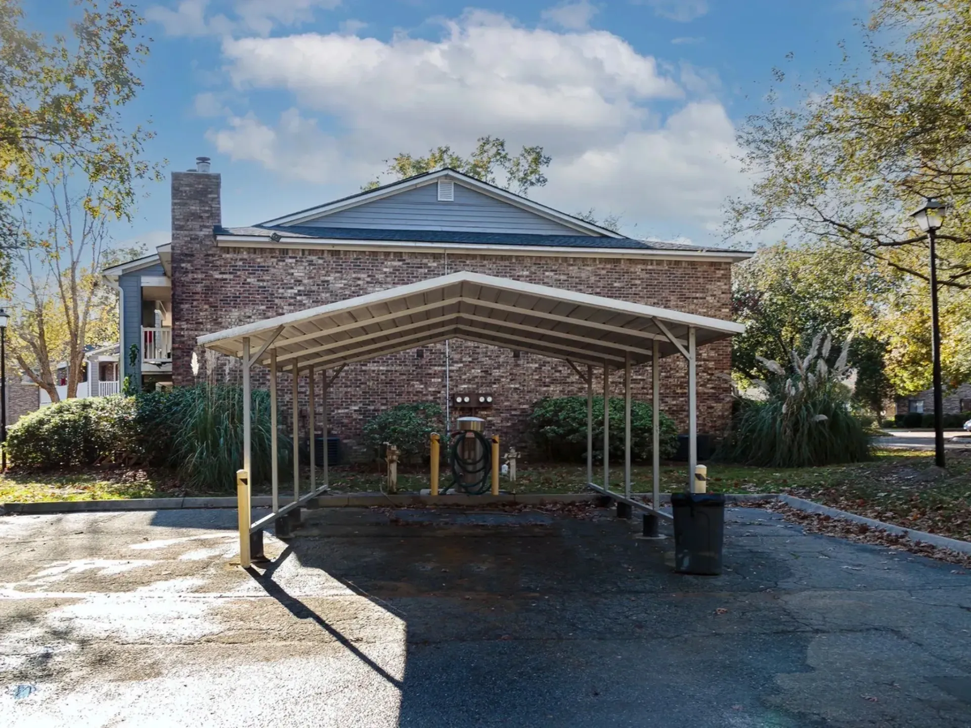 Carport area with green plants and a brick building in the background