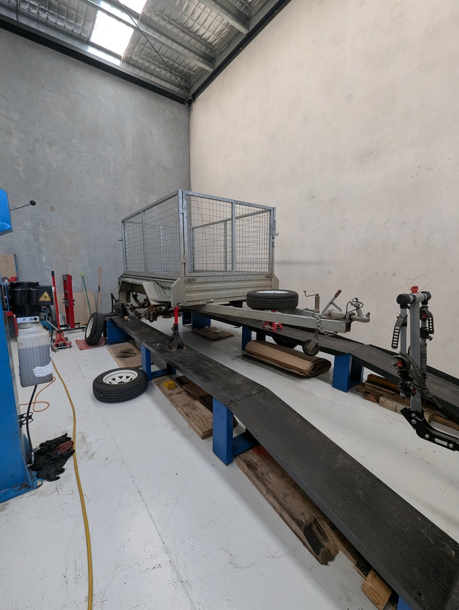 A trailer on a lift in a workshop, grey walls, metal cage, spare tire on floor. — Caravan and Trailer Clinic Geelong in Breakwater, VIC