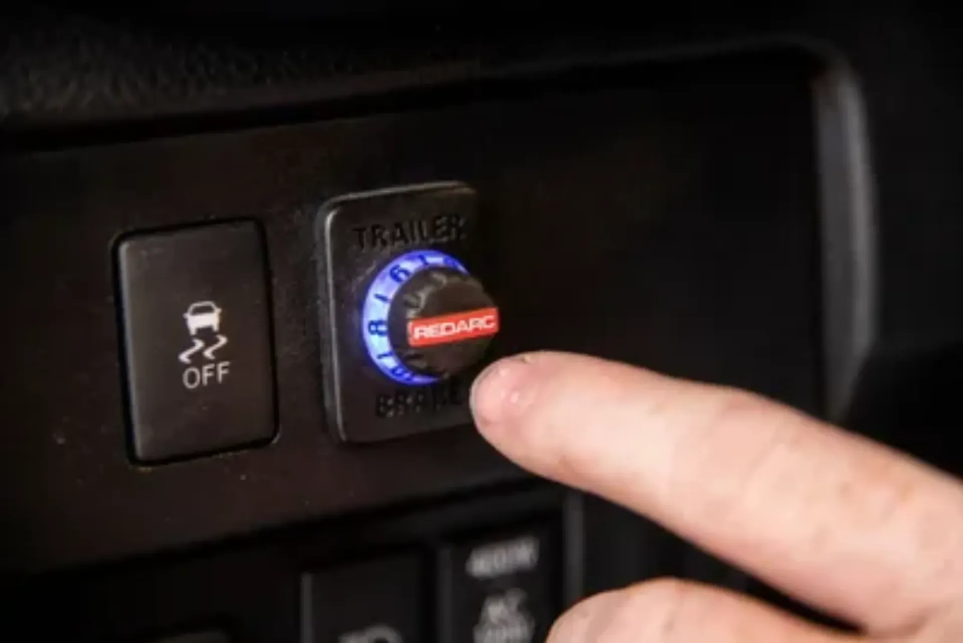 A finger presses a trailer brake control dial in a car. The dial is labeled 