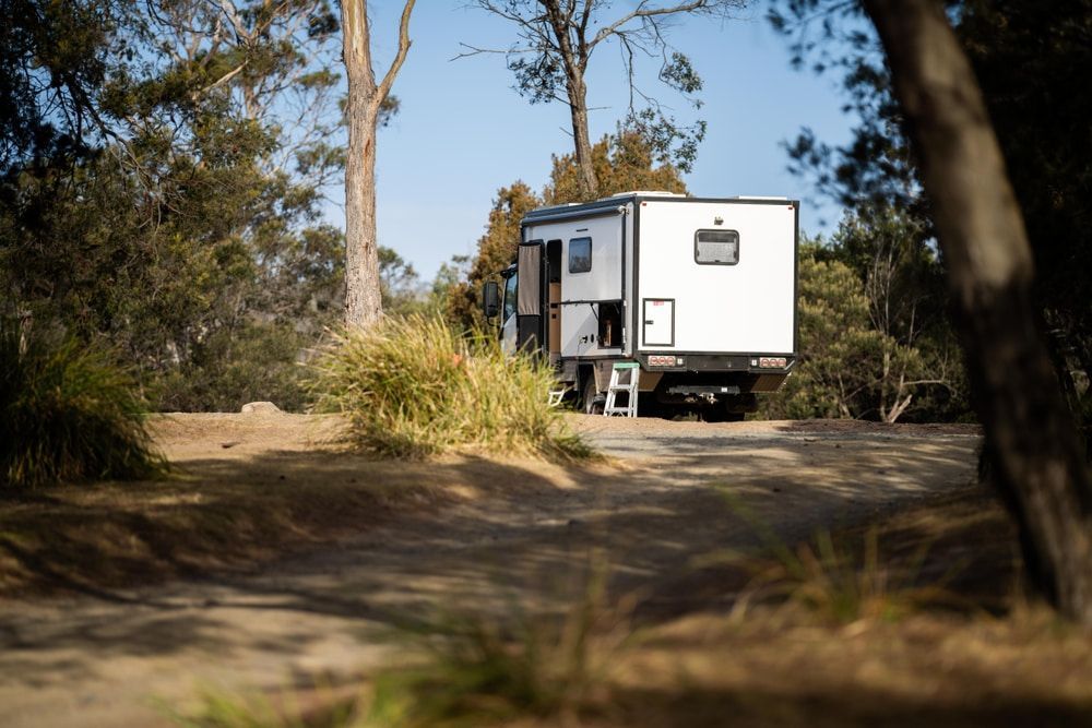 White campervan parked on a dirt road in a wooded area. — Caravan and Trailer Clinic Geelong in Breakwater, VIC