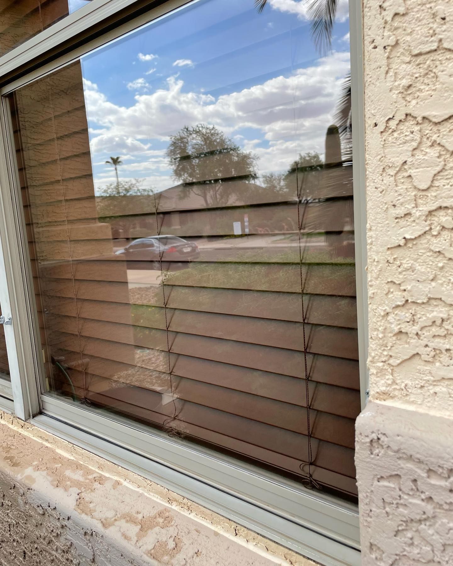 A window with blinds on it and a reflection of a house in the window.