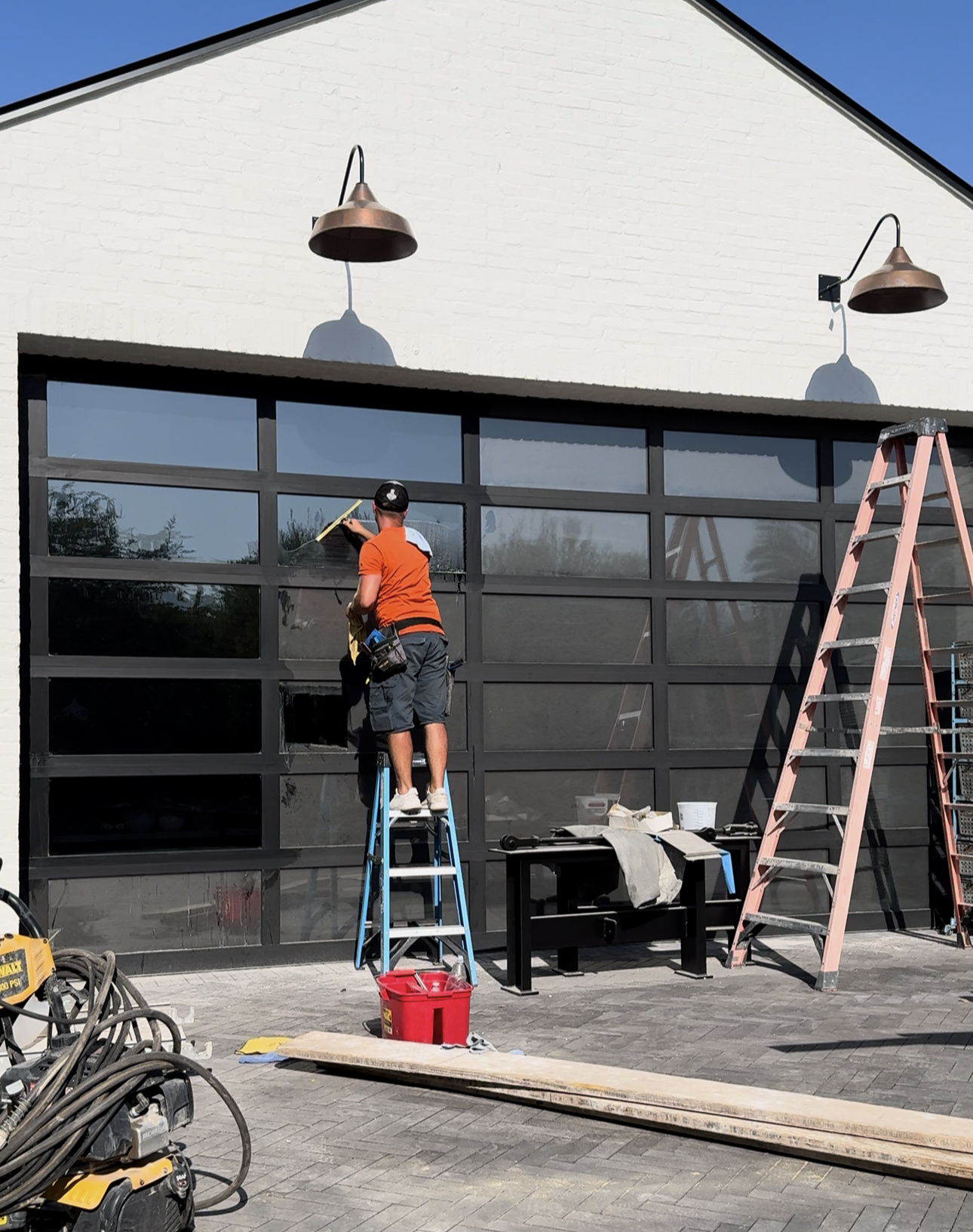 Person cleaning glass garage door, using a squeegee, with ladders and tools nearby.