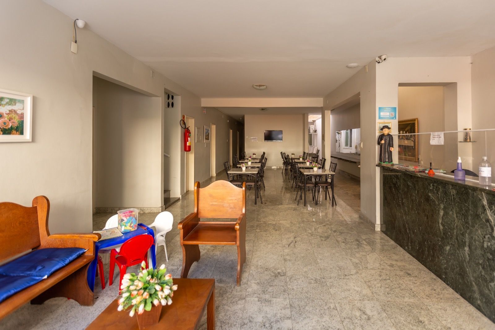 Hall de entrada de um hotel com piso de mármore, móveis de madeira, uma pequena área de recreação infantil e um balcão de recepção.