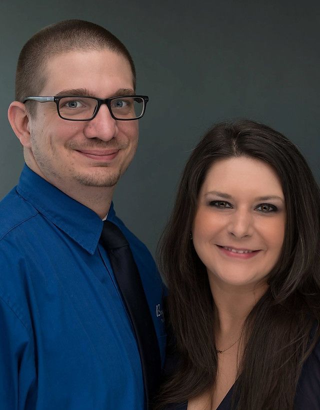 A man and a woman are posing for a picture together . the man is wearing glasses and a blue shirt.