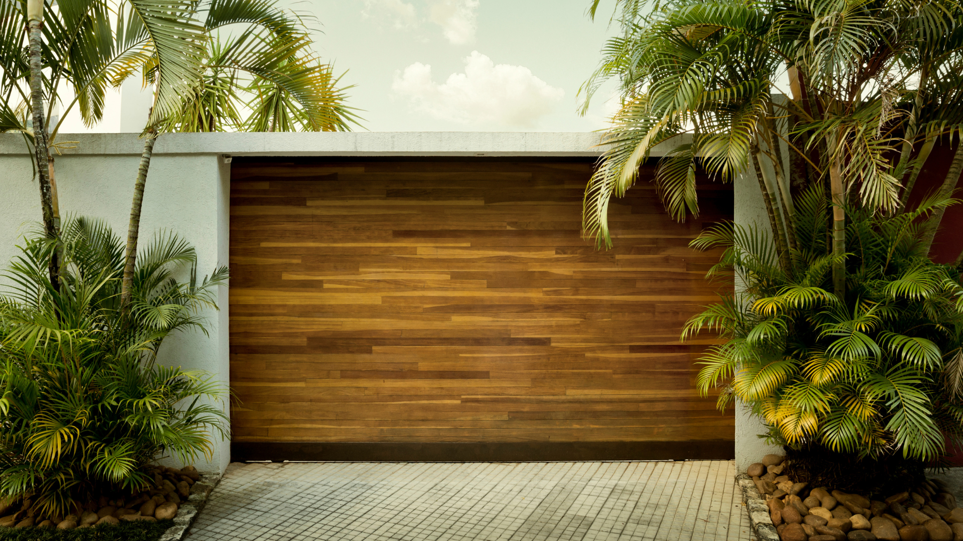 A wooden garage door is surrounded by trees and bushes.
