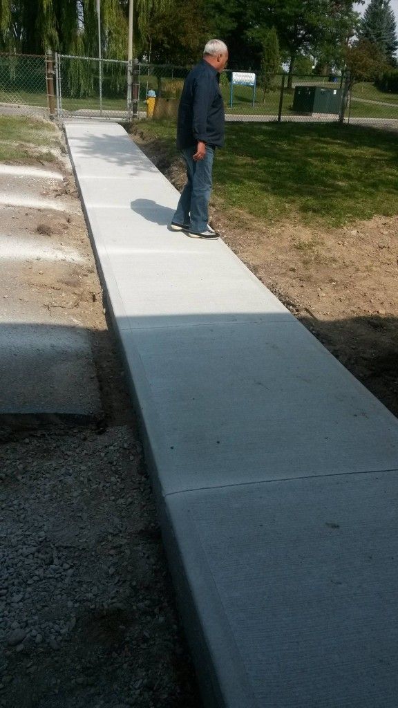 A man is standing on a concrete walkway in a park.