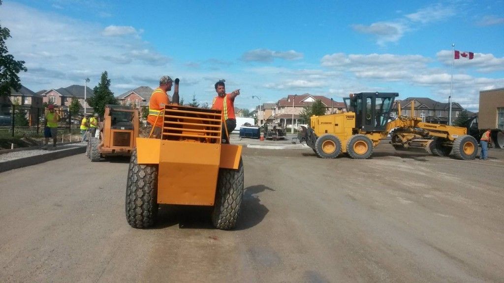 Construction workers are working on a road with a canadian flag in the background