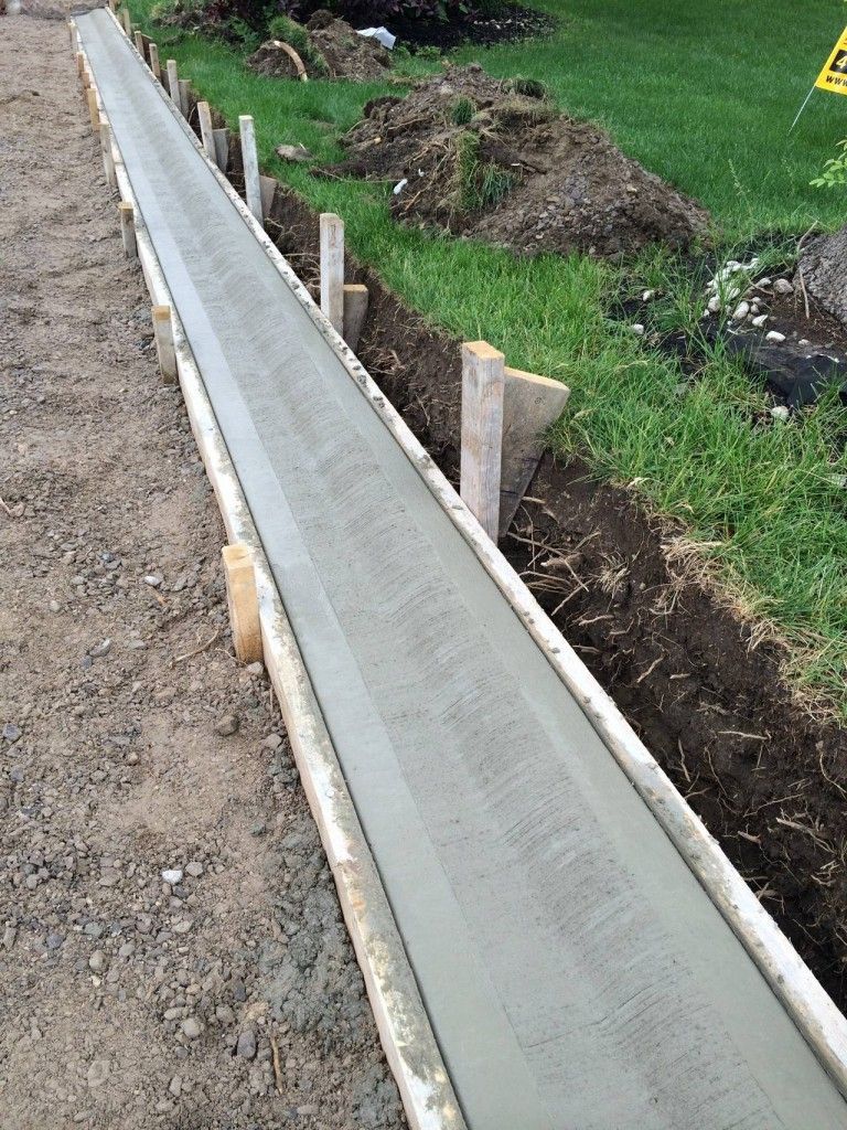 A long piece of concrete is being poured into a trench.