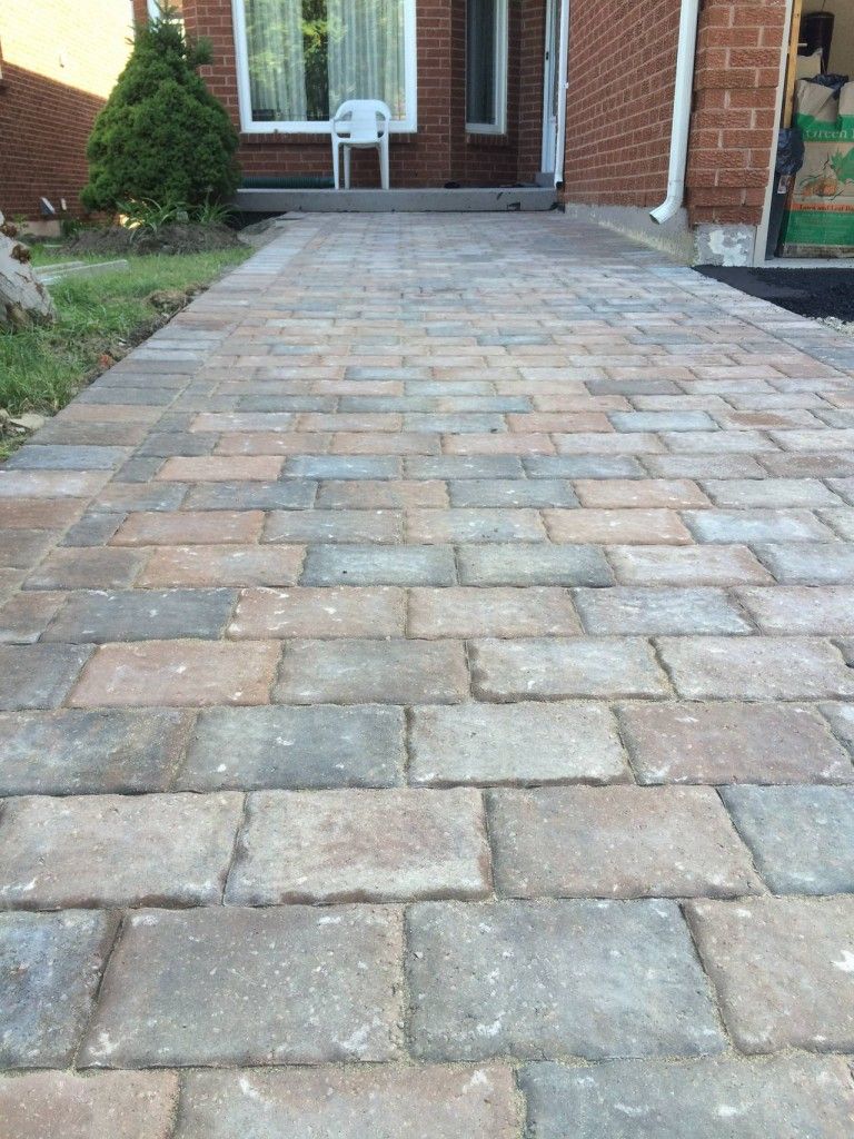 A brick walkway leading to a brick house with a white chair.