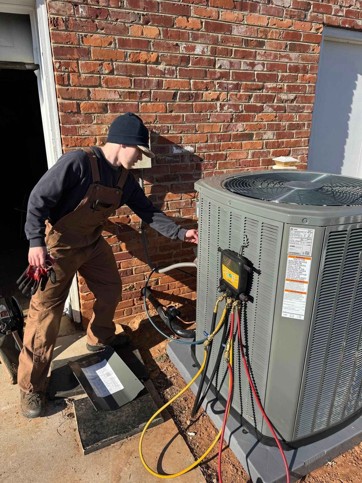 Technician servicing an outdoor HVAC unit with tools beside a brick wall