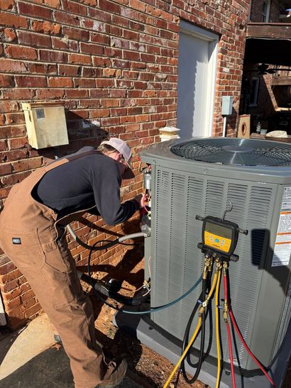 Worker servicing HVAC unit beside a brick building with electrical tools and cables.