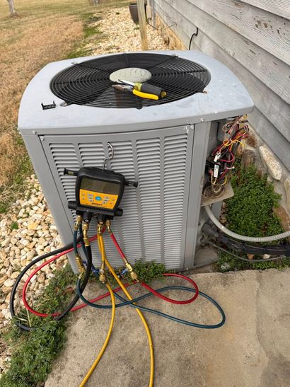 Outdoor AC unit with gauge manifold and hoses attached during servicing outside a house.
