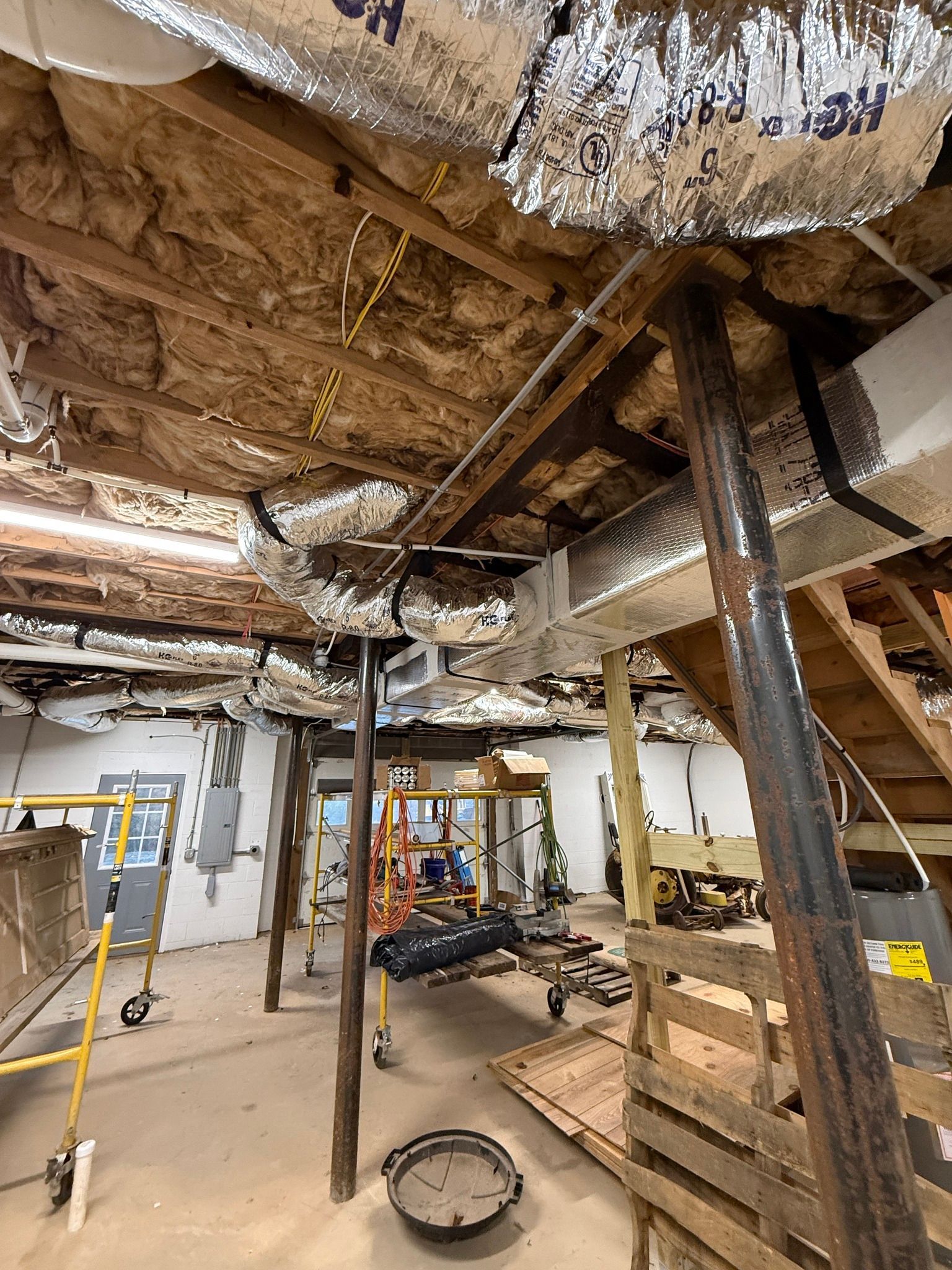 Interior of a damaged building with exposed ceiling insulation, wooden supports, and construction debris on the floor