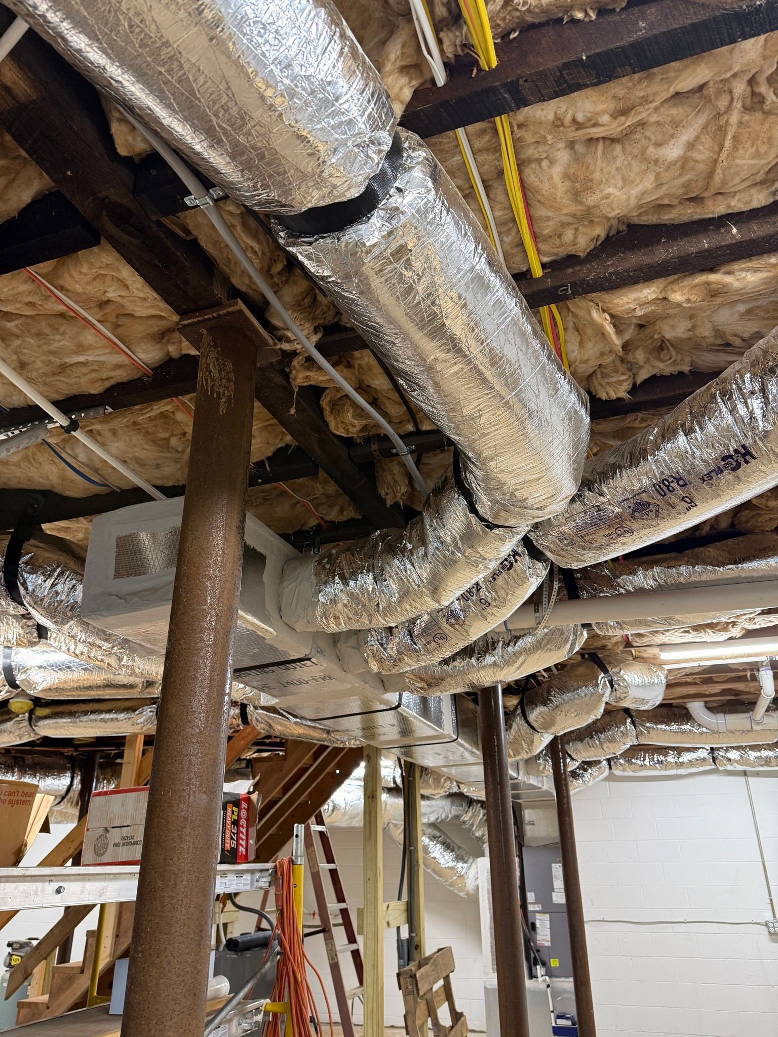Exposed basement ceiling with insulated ductwork, pipes, and support posts in a utility area