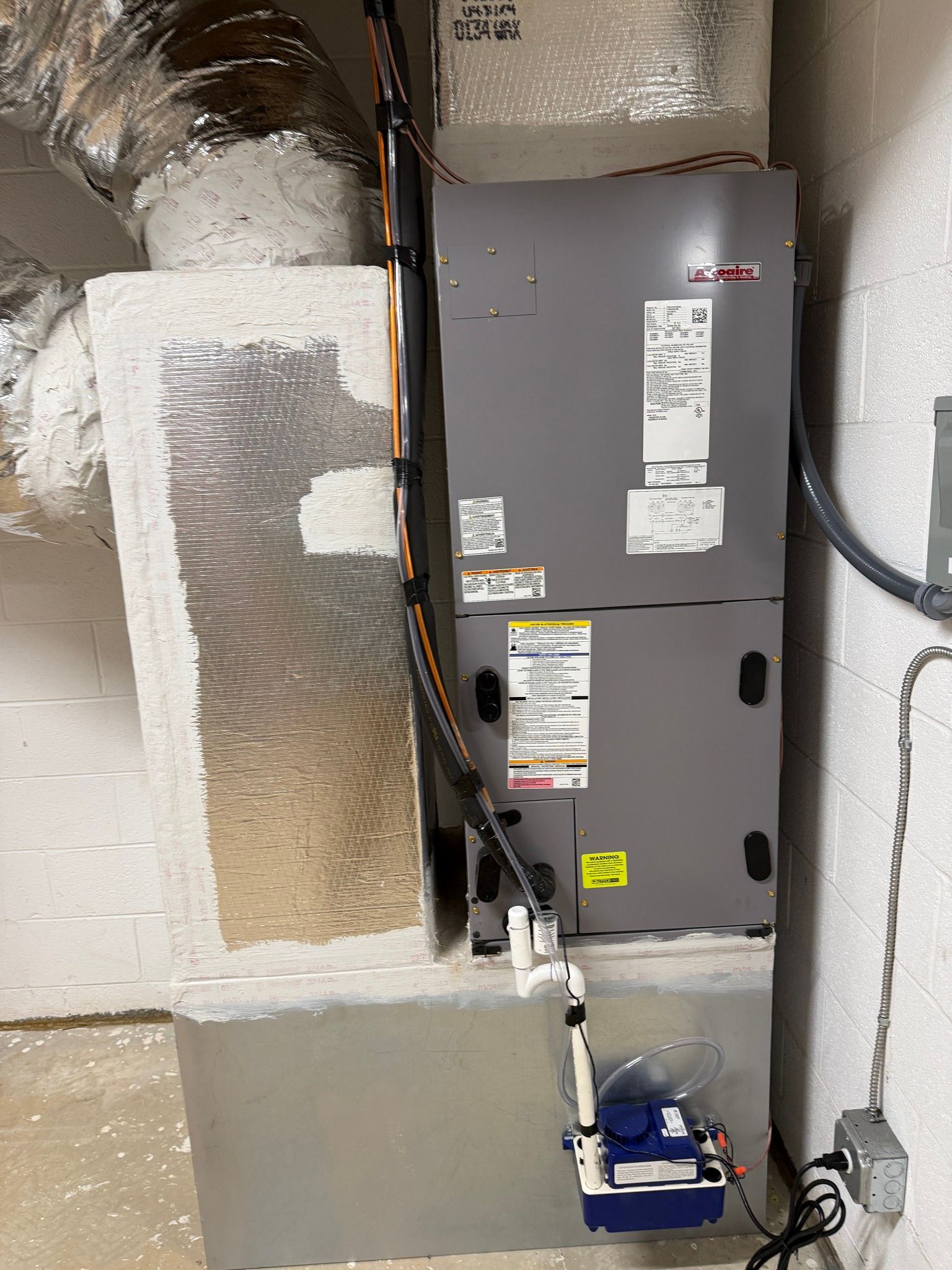 Utility closet with gray HVAC/furnace unit, exposed ducts, and a blue condensate pump on the floor.