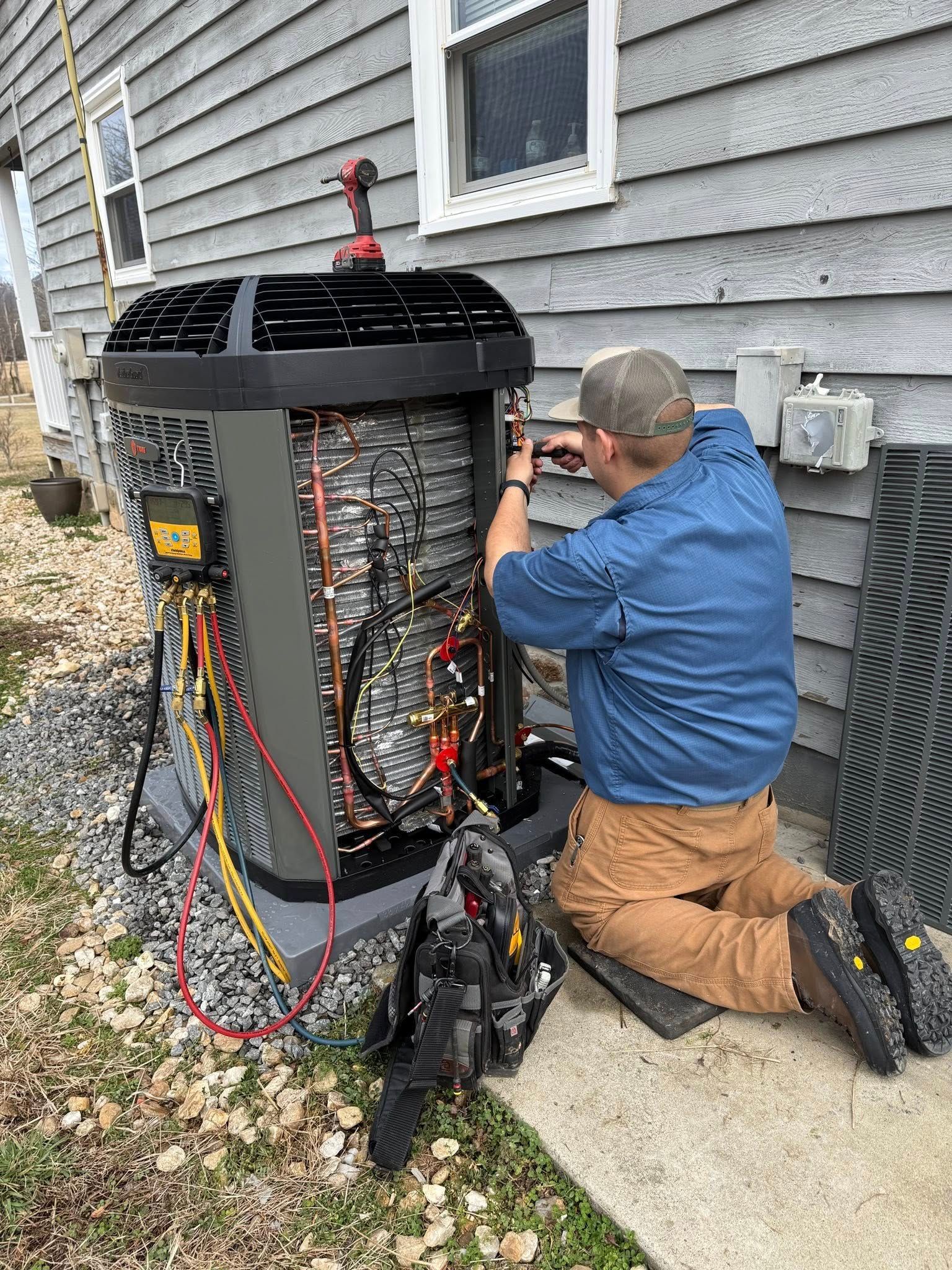 Technician kneeling beside a home HVAC unit, working on exposed wiring and components outdoors