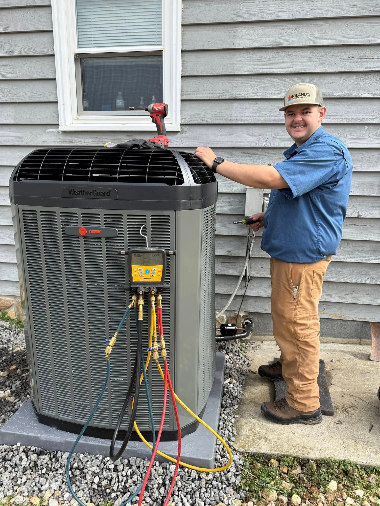 Technician servicing an outdoor air conditioner unit beside a house, with gauges and hoses attached.