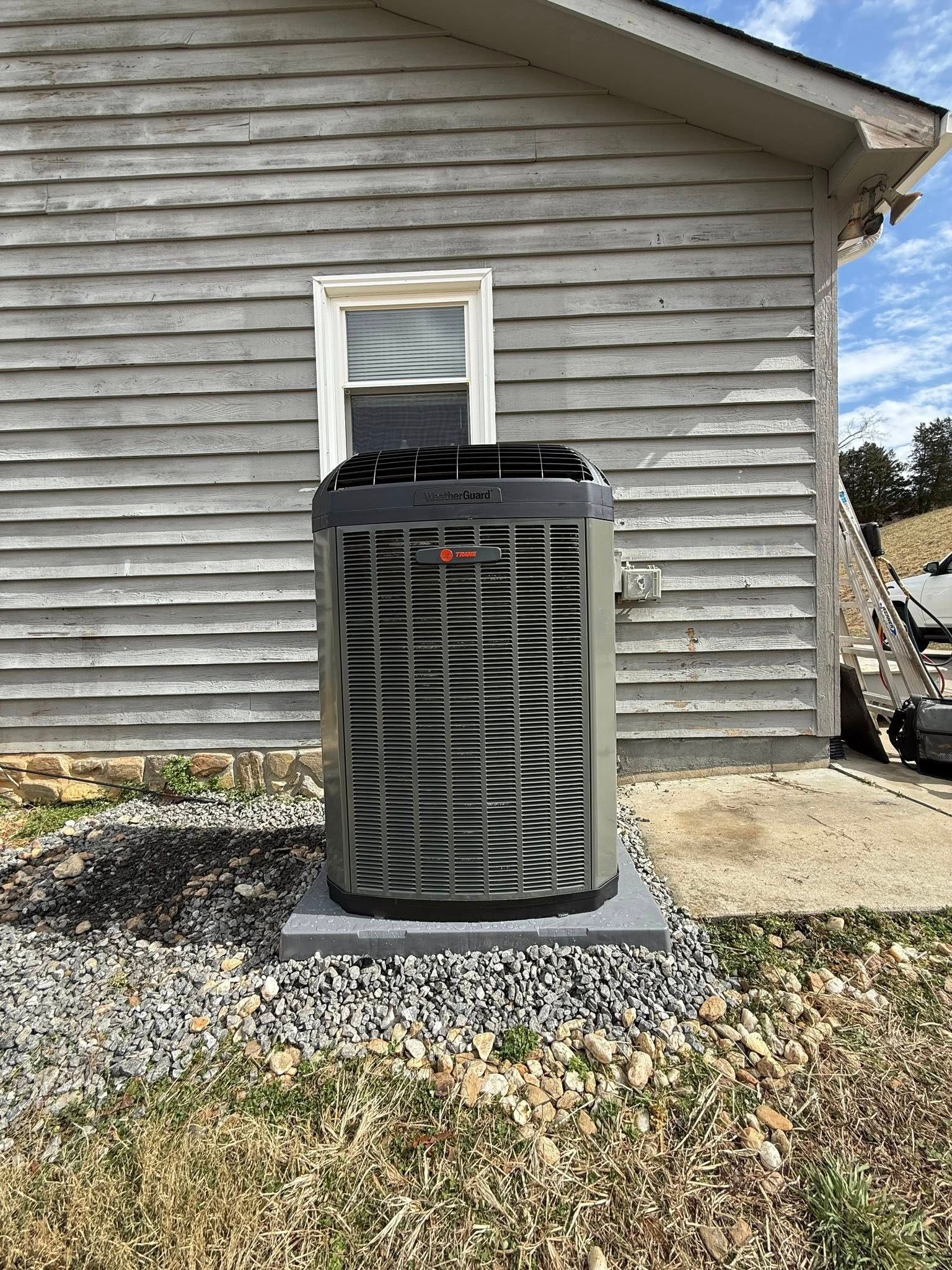 Outdoor air conditioner unit on a concrete pad against a gray-sided house