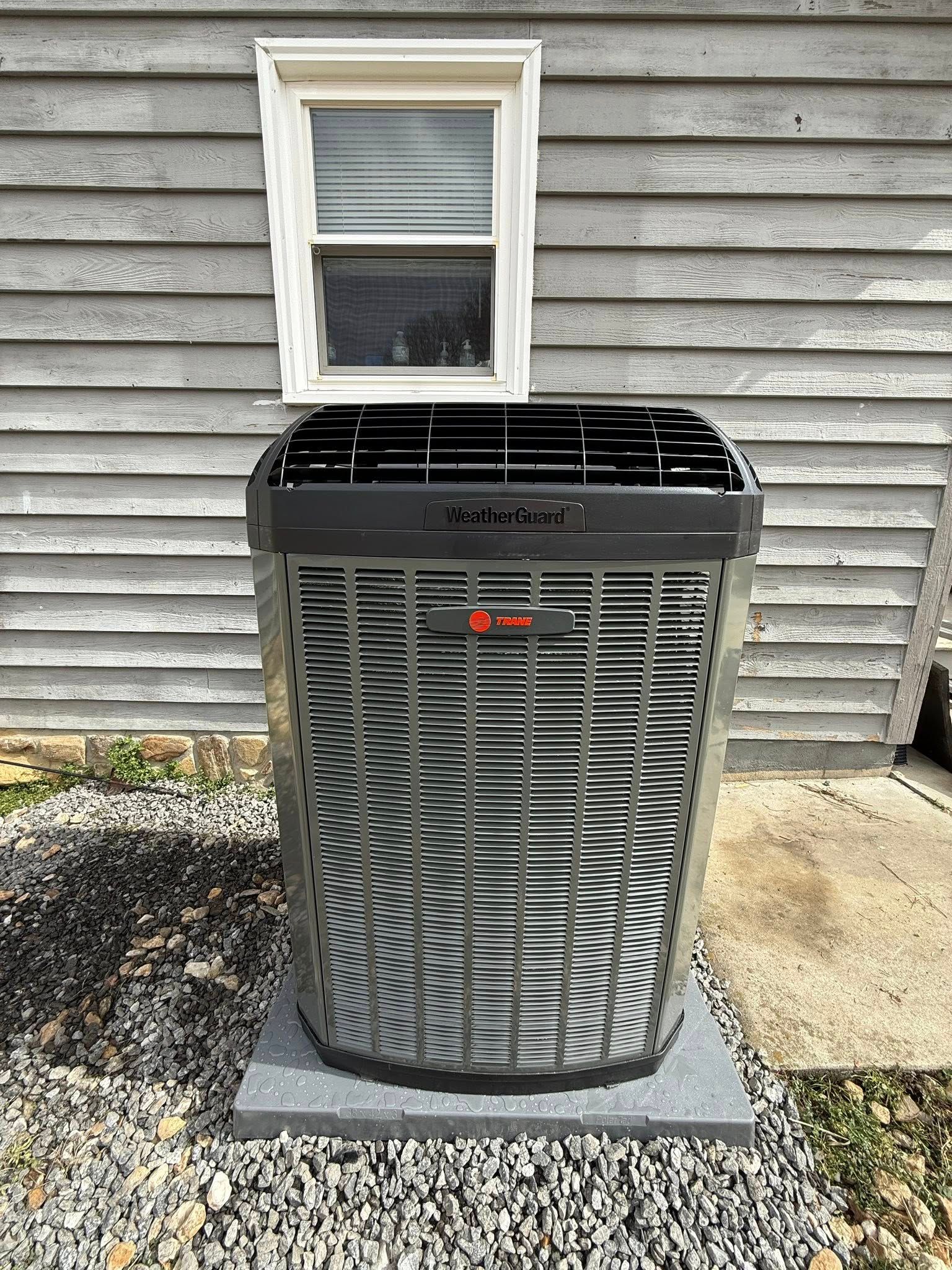 Outdoor air conditioner unit beneath a window against gray siding.