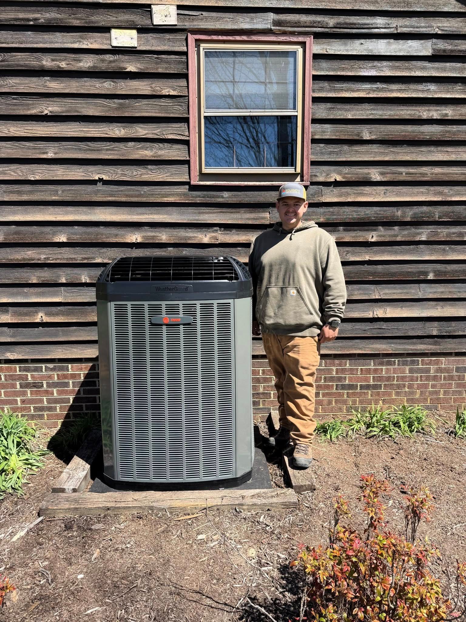 Man standing beside a large outdoor HVAC unit against a wooden building wall.