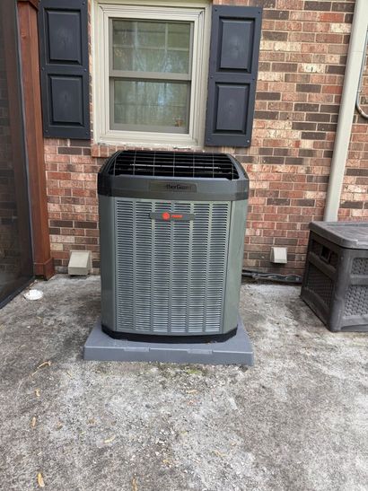 Outdoor air conditioner unit against a brick wall beneath a window with black shutters