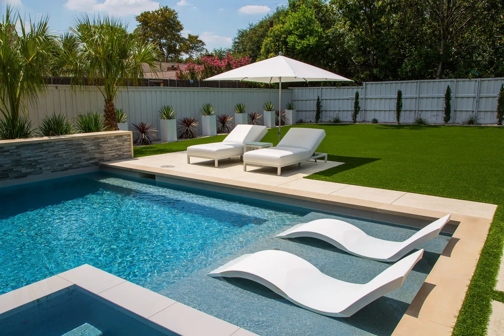 Poolside scene: pool with white lounge chairs, umbrella, and green lawn.