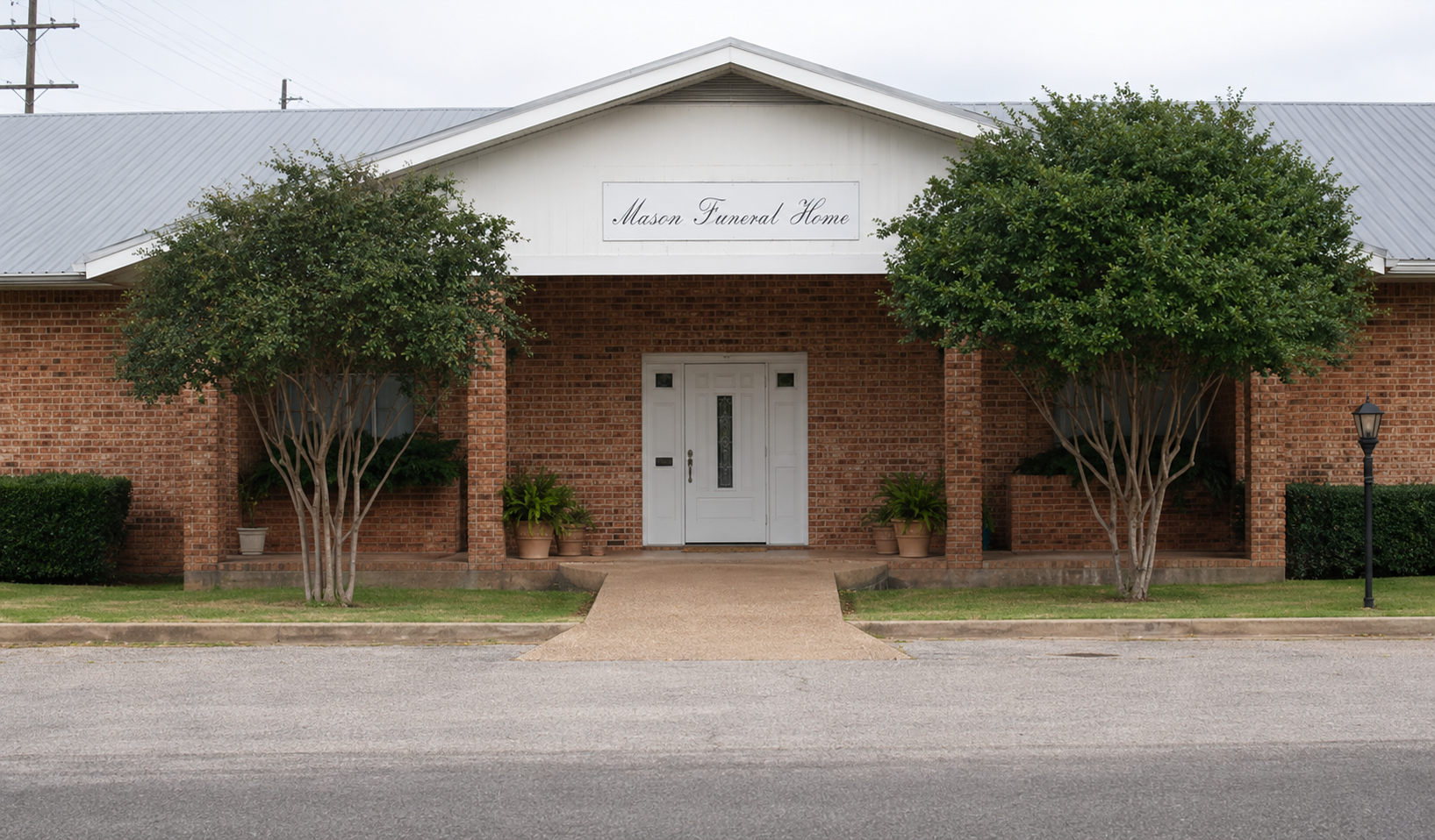 Brick building with white entrance and two trees in front, viewed from a parking lot