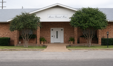 Brick building with white entrance and two trees in front, viewed from a parking lot