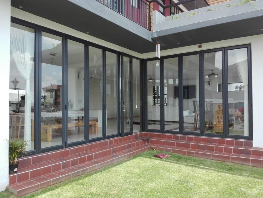 Black framed glass doors on a house corner, brick steps, and green lawn.