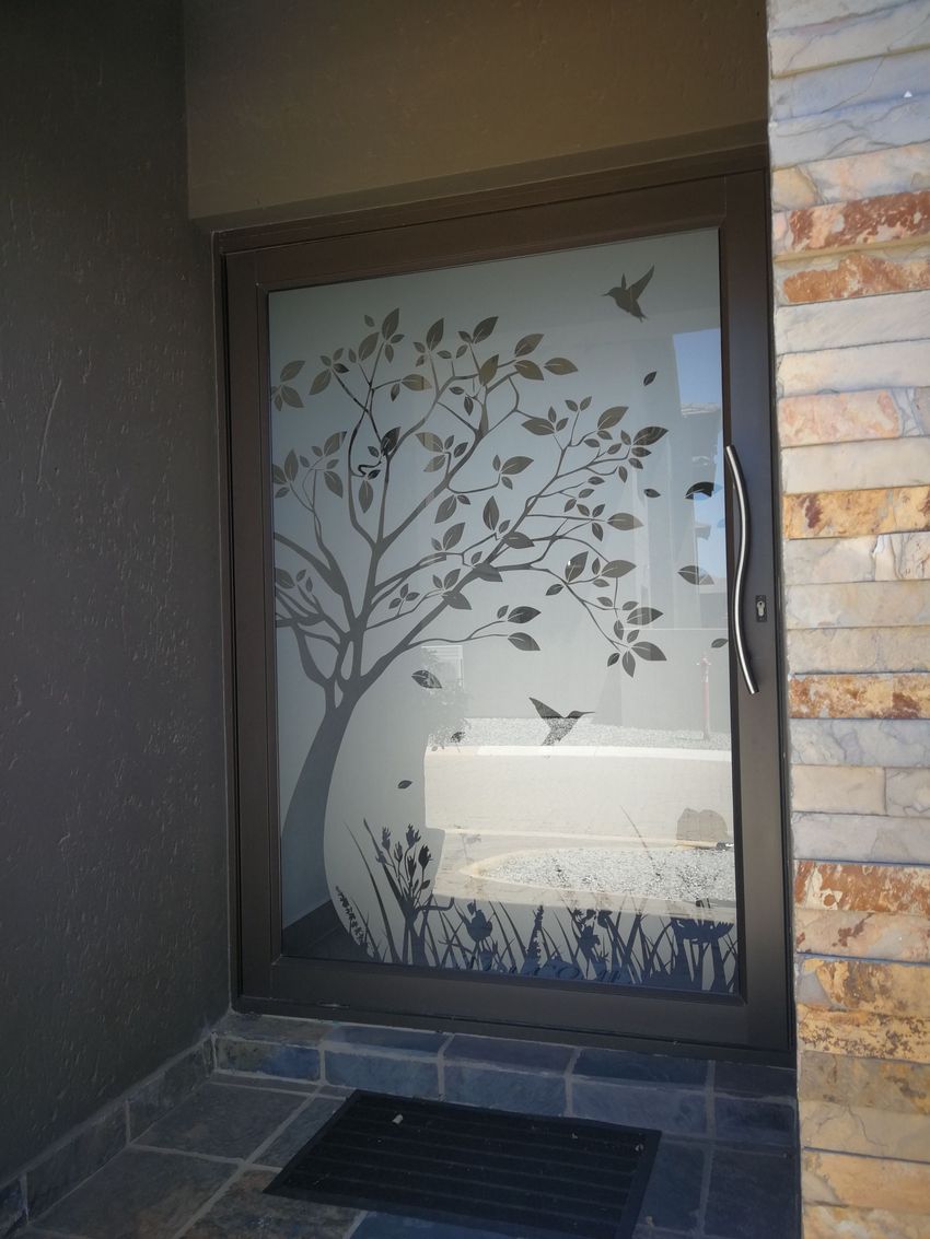 Frosted glass door with tree and birds design; in an entryway with stone and dark gray walls.