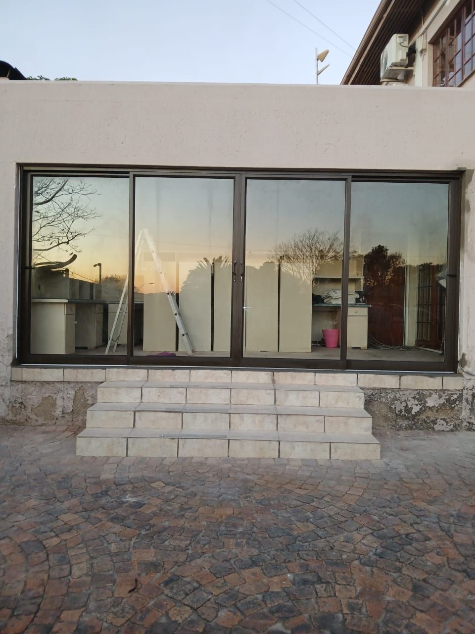 A light beige house with a wooden board covering a window, with two windows on either side.