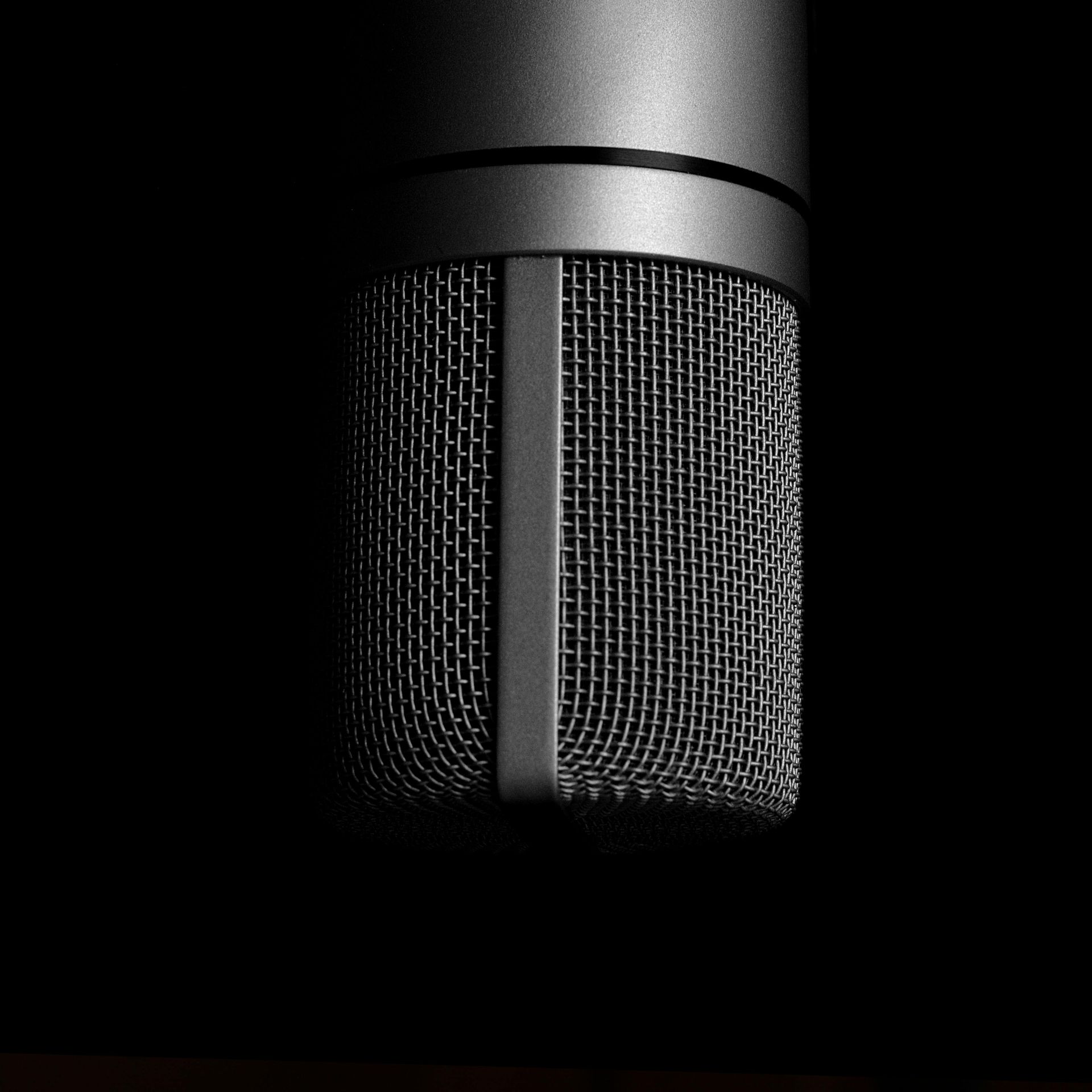 Black studio microphone against a dark background, highlighted with subtle lighting.