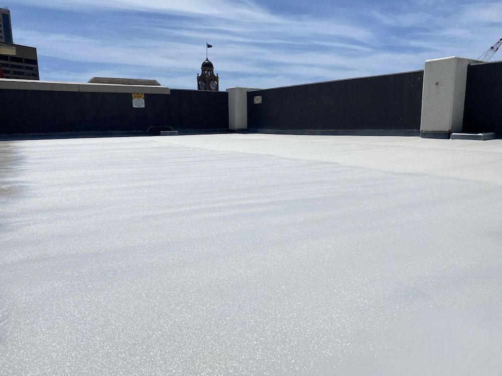 White, reflective roof coating on a flat rooftop with a city backdrop and blue sky. — Unique Waterproofing Solutions in North Rocks, NSW